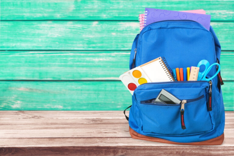 Blue backpack filled with school supplies on wooden surface.