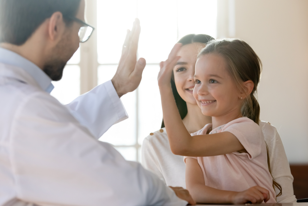 Doctor giving a high-five to a smiling young girl in a clinic.